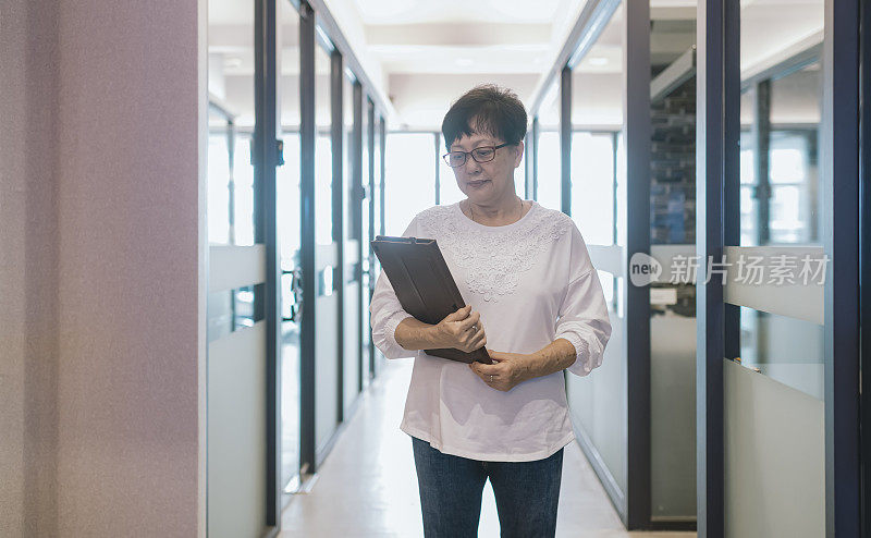 a working senior woman carrying a digital tablet walking in the corridor of the office going to attend a business meeting